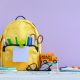 Mochila amarilla con útiles escolares y un autobús de juguete