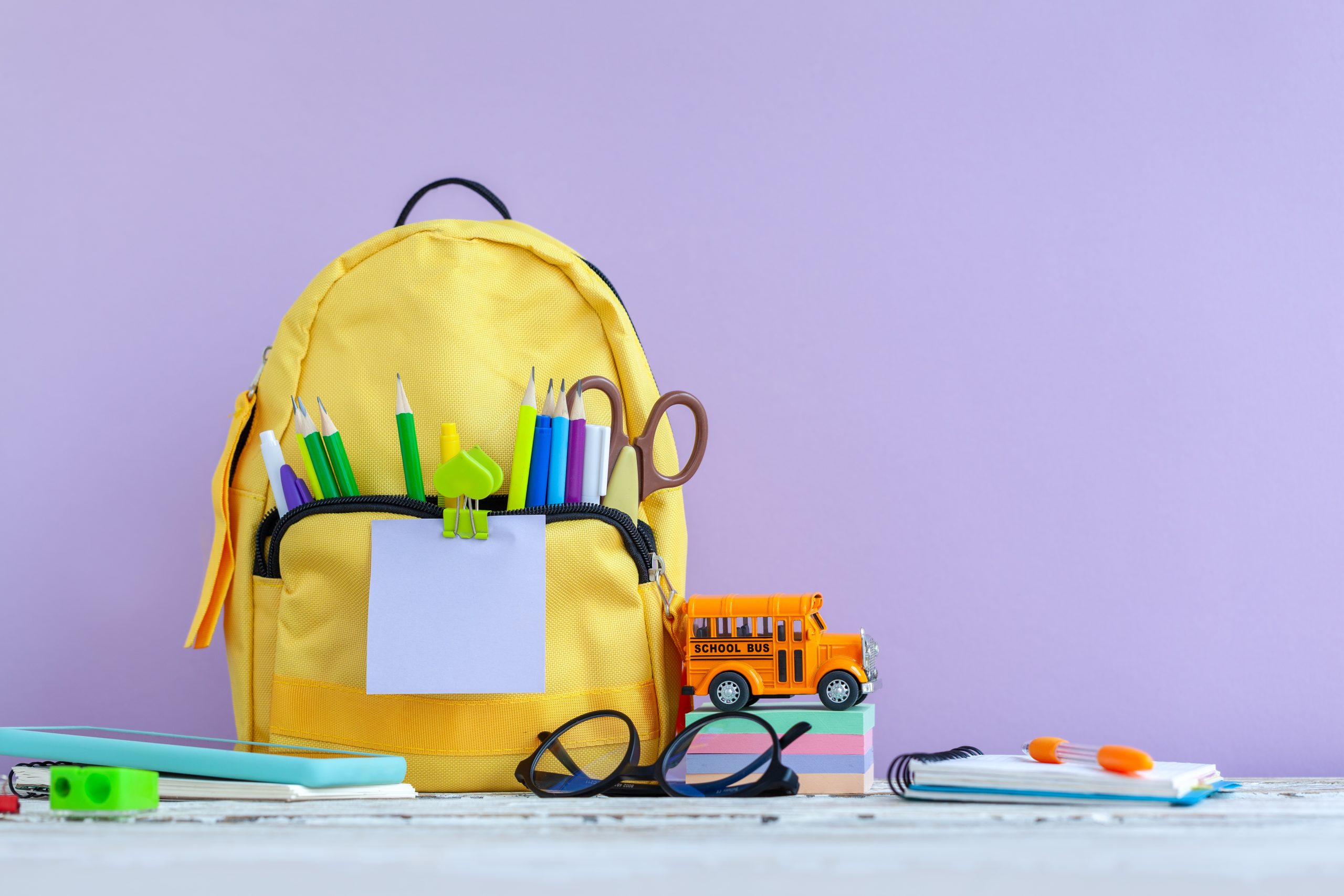 Mochila amarilla con útiles escolares y un autobús de juguete